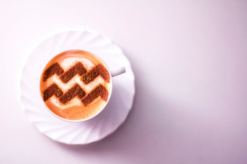 a cup of cappuccino coffee with a pattern of the aquarius aquarius zodiac sign on milk foam